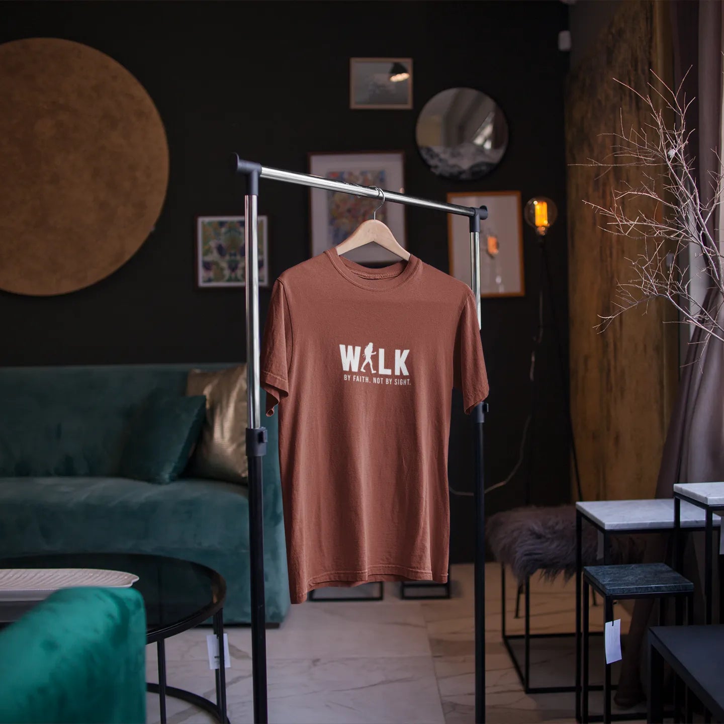 Brown t-shirt with 'WALK' printed on it hanging on a stand in a room with green sofa and decor.
