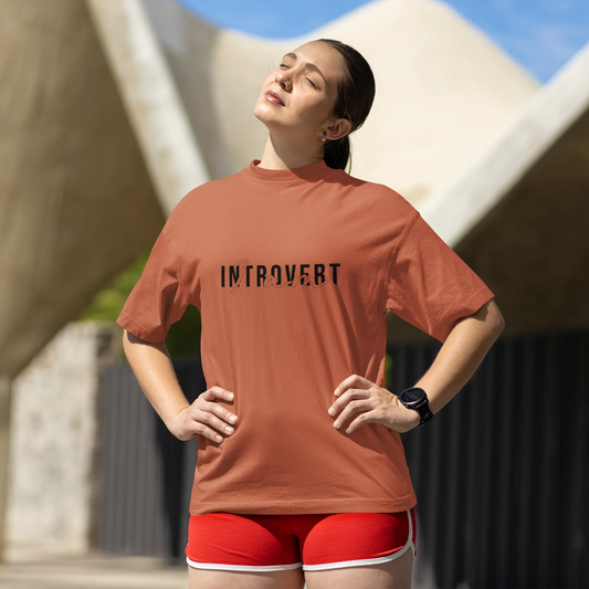 Person wearing a brown t-shirt with 'INTROVERT' printed on it, standing outdoors.