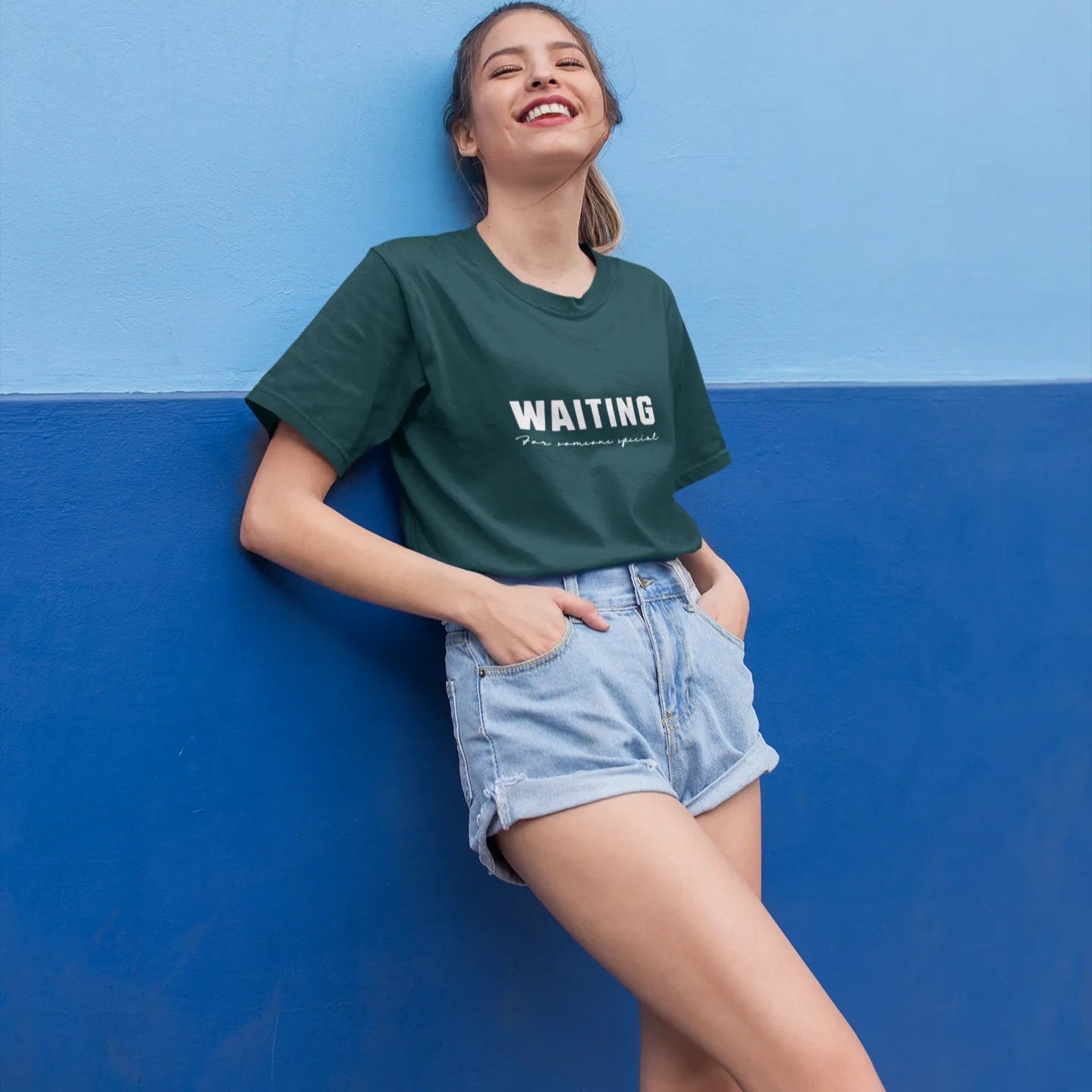 Person wearing a green t-shirt with 'WAITING' text against a blue wall