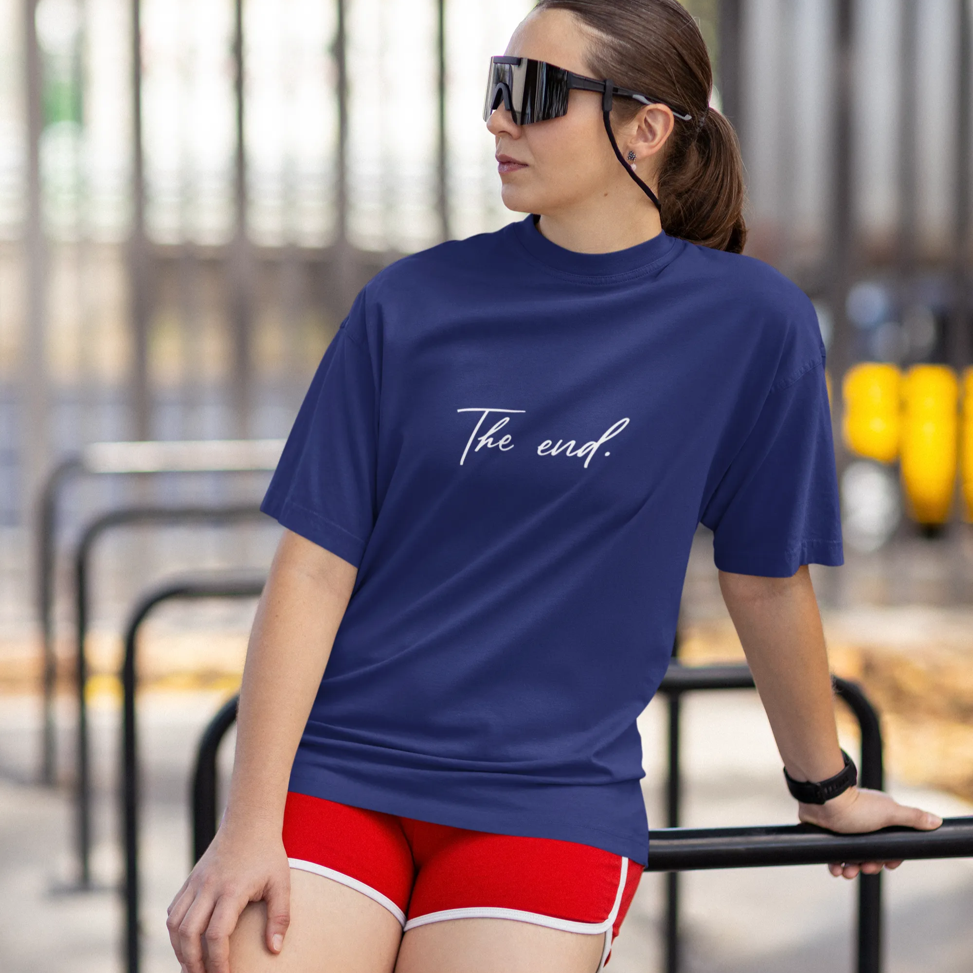 Woman wearing a blue shirt with 'The End.' text and red shorts outdoors.