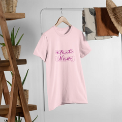 Pink t-shirt with text on a hanger against a white wall with wooden shelves and plants.