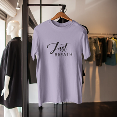 Light purple t-shirt with 'Just Breath' text on a hanger in a store setting.