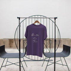 Purple t-shirt with text on a black metal stand against a white wall.