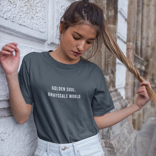 Woman wearing a dark gray t-shirt with 'Golden Soul, Grayscale World' text, standing against a stone wall.
