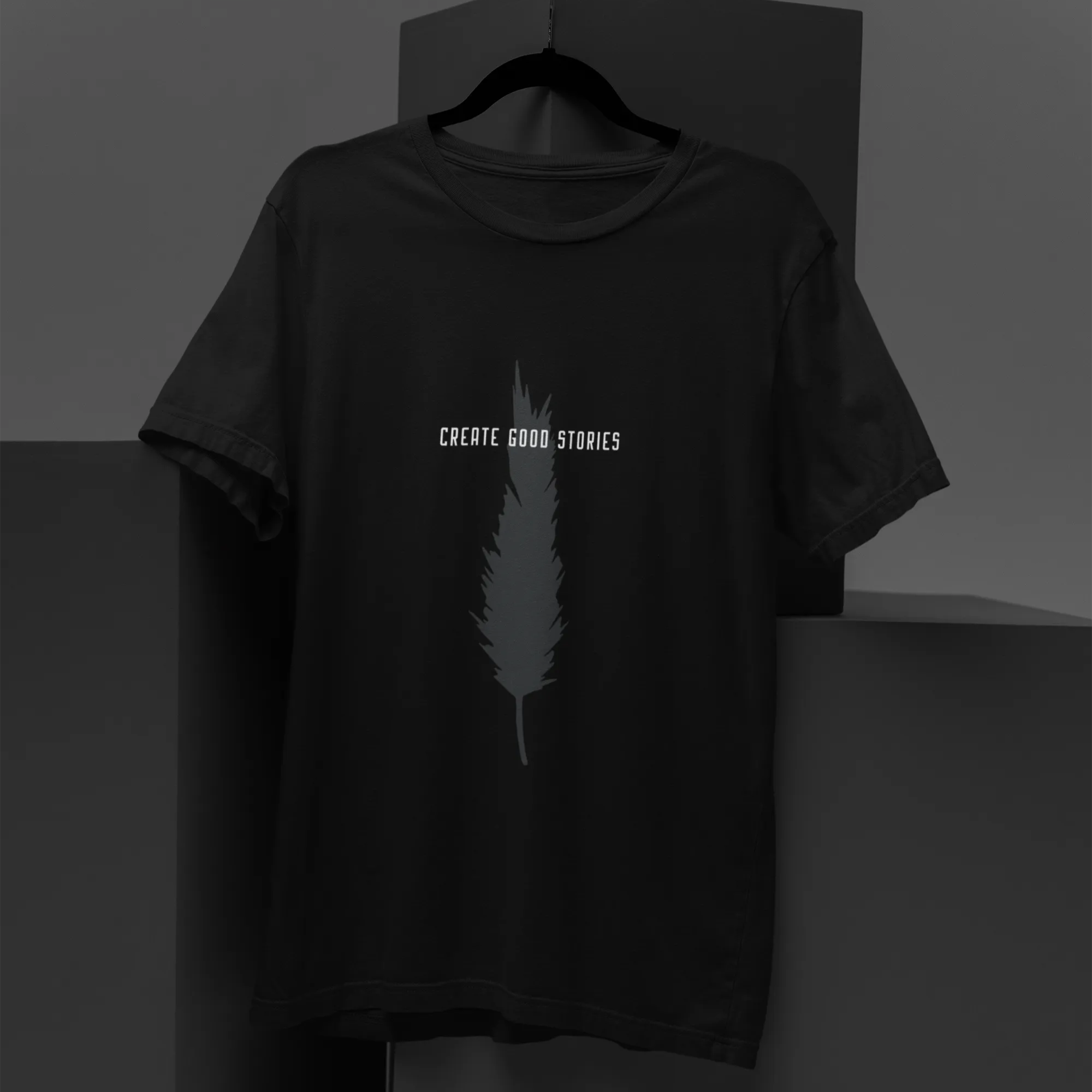 Black t-shirt with feather graphic and 'Create Good Stories' text on a dark background