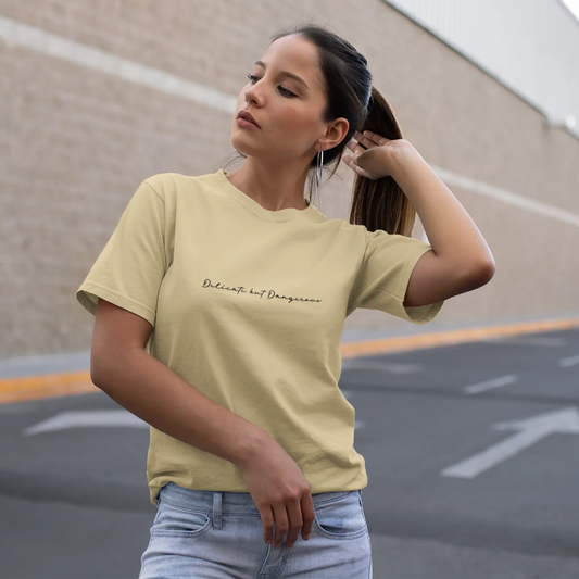 Woman wearing a light yellow t-shirt with text, standing in an outdoor setting.