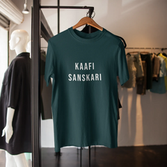 Green t-shirt with 'KAAFI SANSKARI' text on a hanger in a store setting.