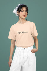 Woman wearing a beige t-shirt with 'Whatever' text and white pants on a green background
