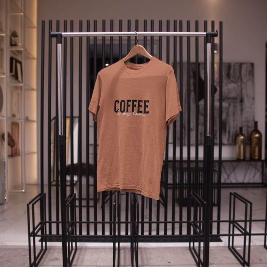 Brown t-shirt with 'COFFEE' text on a hanger against a black metal rack.