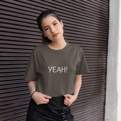 Woman wearing a gray t-shirt with 'YEAH!' text standing against a textured wall.