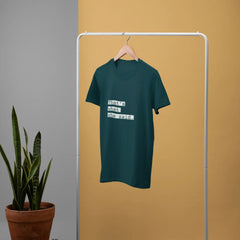 Green t-shirt on a hanger against a mustard yellow wall with a plant and basket in the foreground.