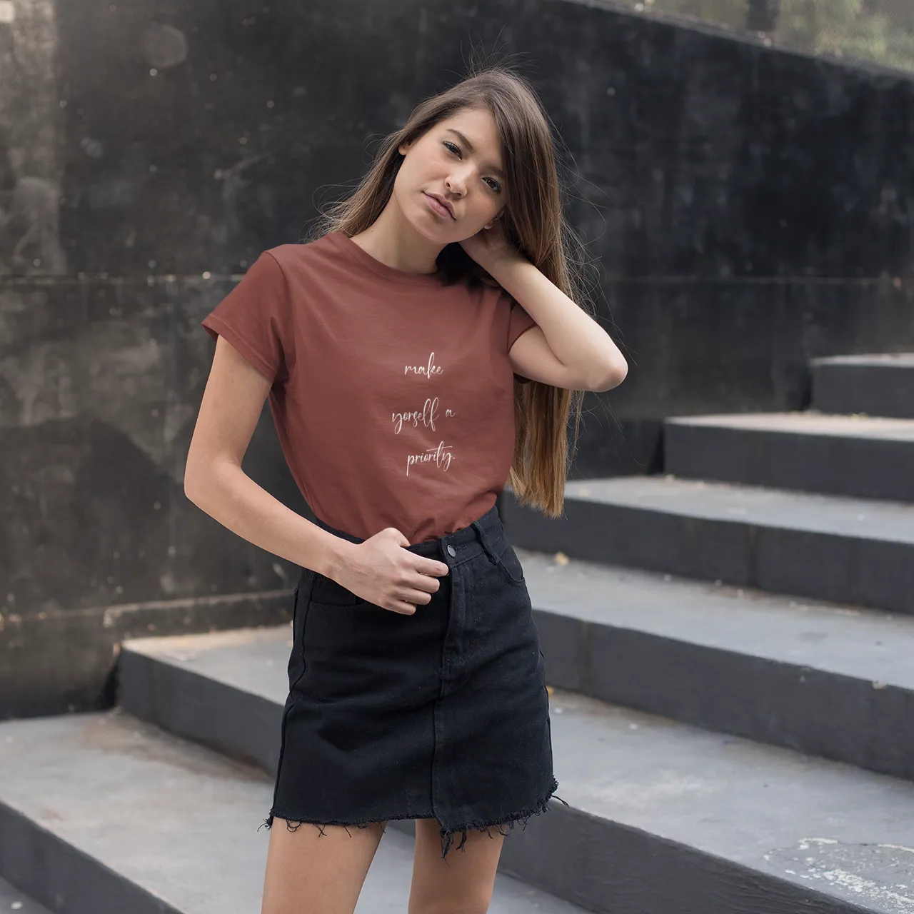 Woman wearing a brown t-shirt with text on it, standing on stone steps.