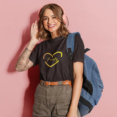 Woman wearing a black t-shirt with a yellow heart design, holding a blue backpack against a pink background