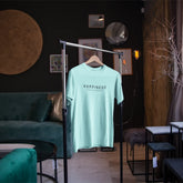 Light blue t-shirt with 'HAPPINESS' text on a hanger in a stylish room.