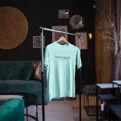 Light blue t-shirt with 'HAPPINESS' text on a hanger in a stylish room.