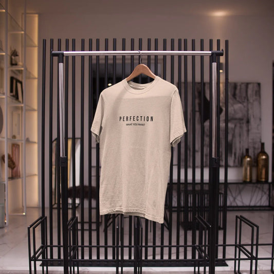 Beige t-shirt with 'PERFECTION' text on a black metal rack in a store setting.