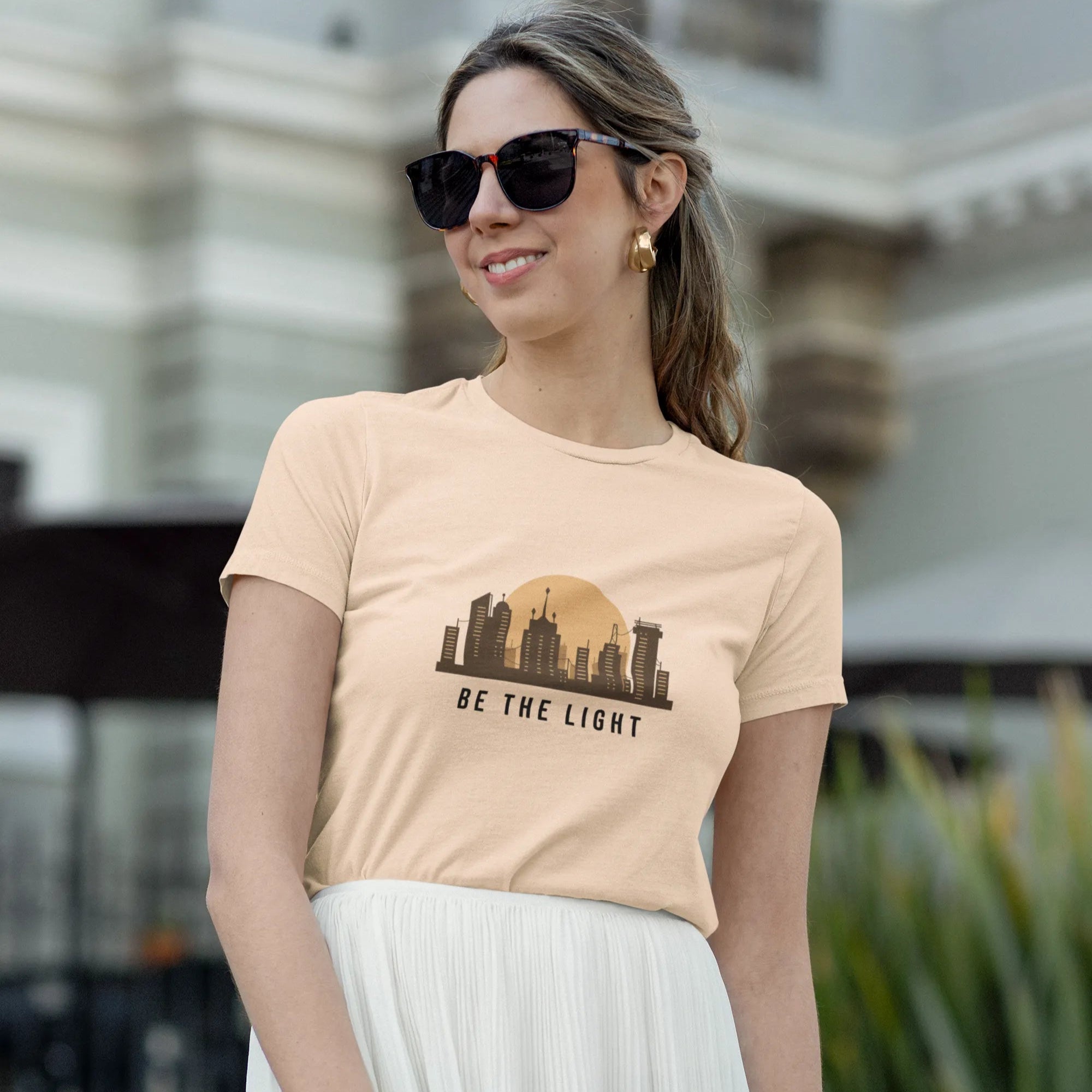 Woman wearing a beige t-shirt with a graphic design and text, standing outdoors.