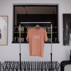 Pink t-shirt with 'Unlimited Adventure' text hanging in a modern interior setting.