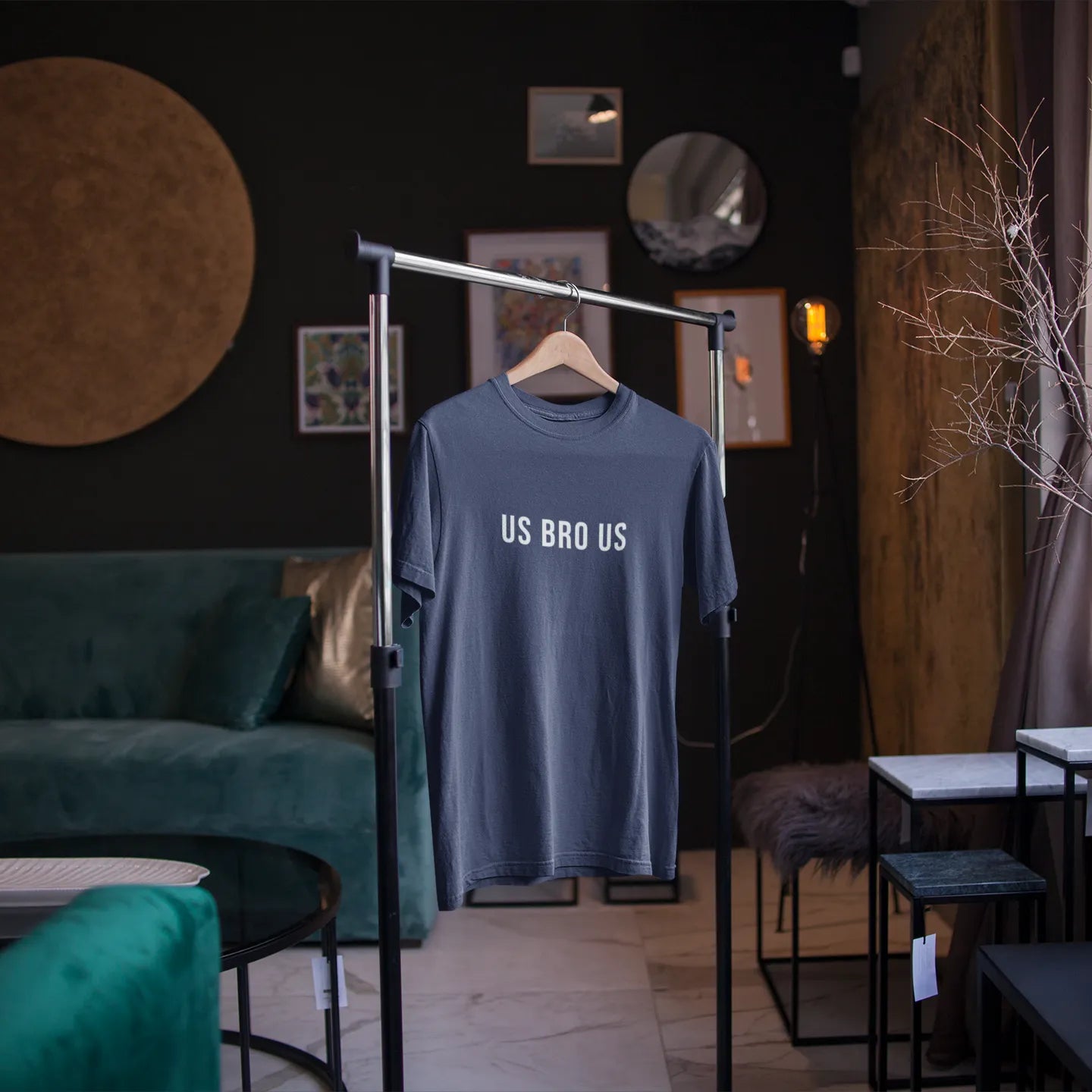 Blue t-shirt with 'US BAD US' text on a hanger in a room with green sofa and decor elements.