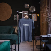 Blue t-shirt with 'US BAD US' text on a hanger in a room with green sofa and decor elements.