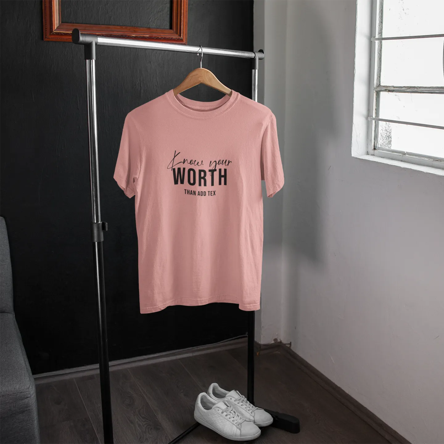 Pink t-shirt with text on a hanger in a room with a window.