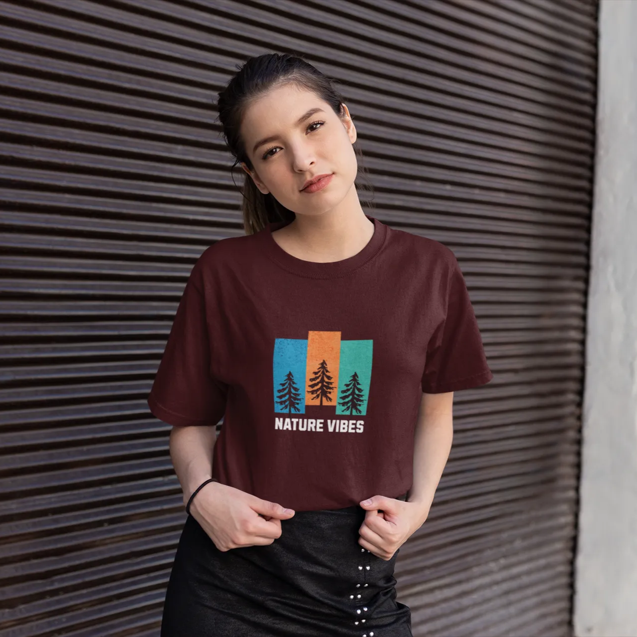 Woman wearing a brown t-shirt with a nature-themed design against a textured wall.