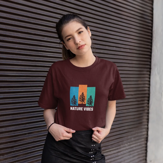 Woman wearing a brown t-shirt with a nature-themed design against a textured wall.
