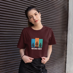 Woman wearing a brown t-shirt with a nature-themed design against a textured wall.