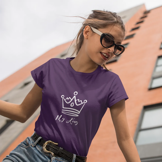 Woman wearing a purple t-shirt with a logo and text, standing in front of a building.