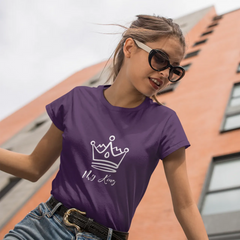 Woman wearing a purple t-shirt with a logo and text, standing in front of a building.