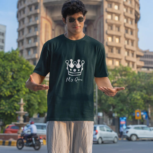 Person wearing a black t-shirt with a logo and text, standing in an urban setting with buildings and trees in the background.