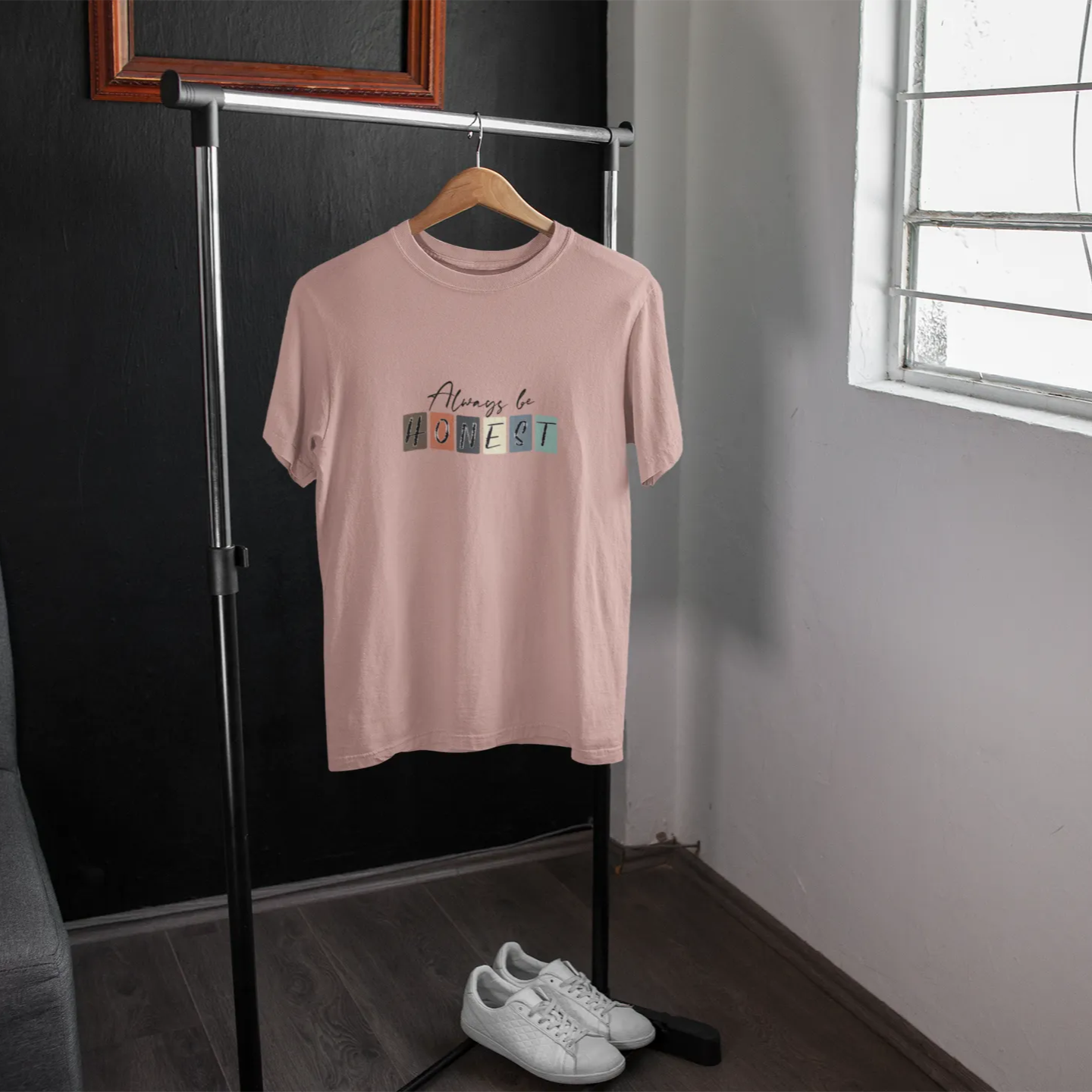 Pink t-shirt with colorful text on a hanger in a room with a window.