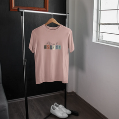 Pink t-shirt with colorful text on a hanger in a room with a window.