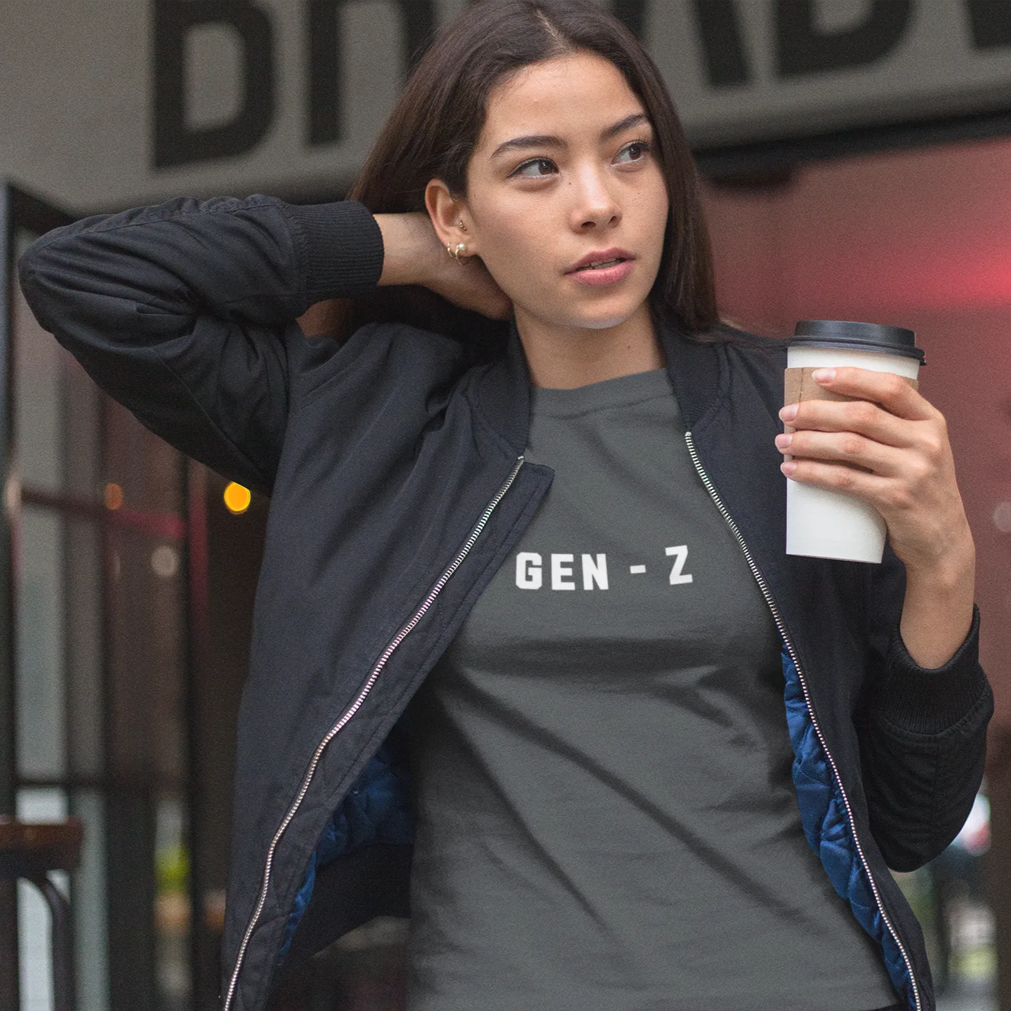 Woman wearing a 'GEN-Z' t-shirt holding a coffee cup outdoors.