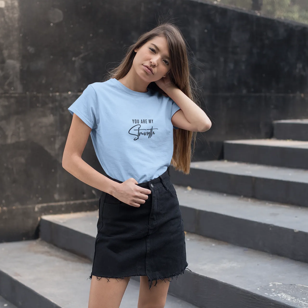 Woman wearing a light blue t-shirt with text on it, standing on steps outdoors.
