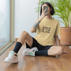 Person sitting on the floor wearing a yellow t-shirt with 'Space is the Place' text.