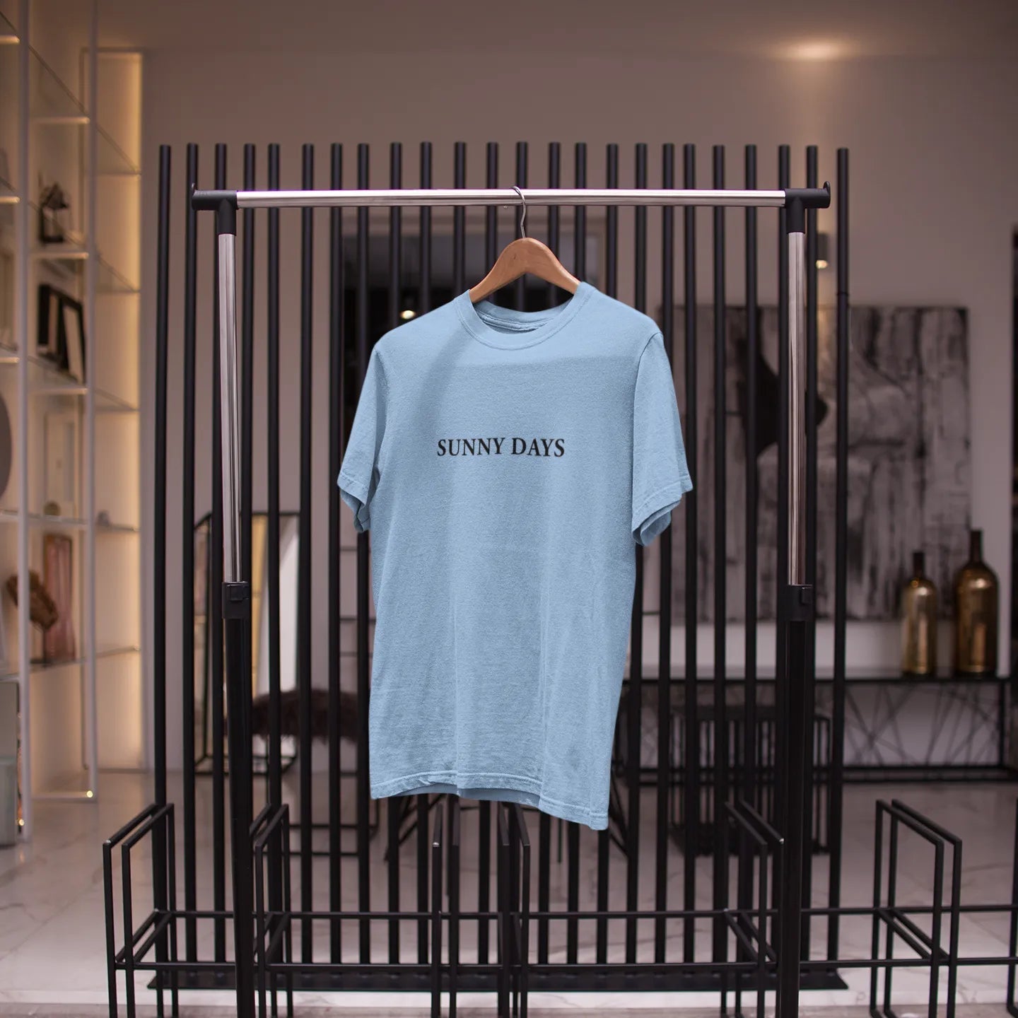 Light blue t-shirt with 'Sunny Days' text on a hanger against a black metal rack.