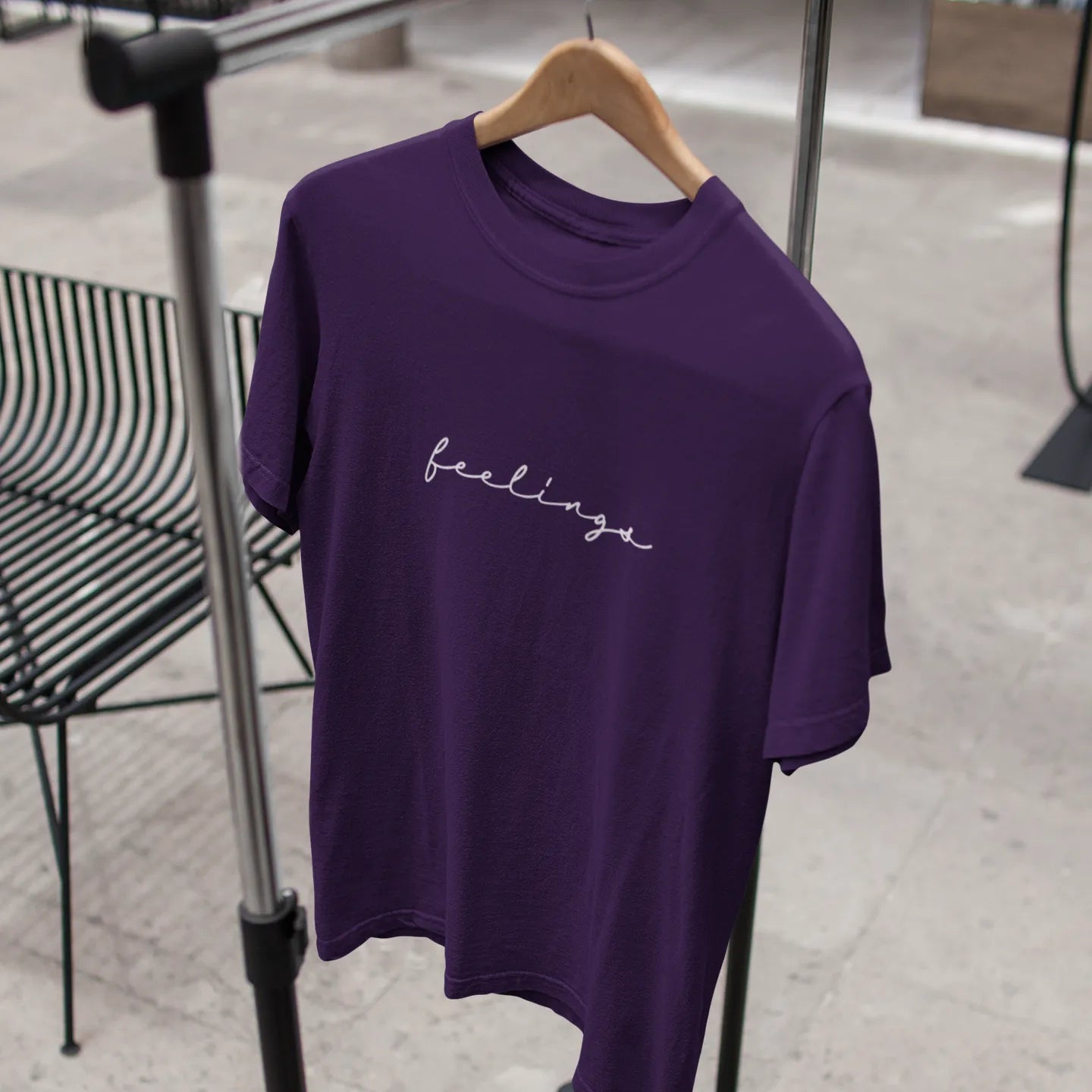 Purple t-shirt with 'feelings' text on a hanger against a neutral background
