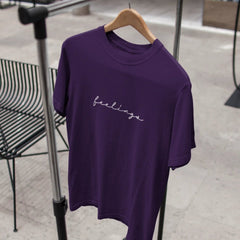 Purple t-shirt with 'feelings' text on a hanger against a neutral background