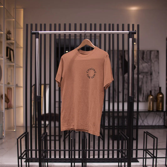 Brown t-shirt on a hanger against a black metal rack in a store setting.