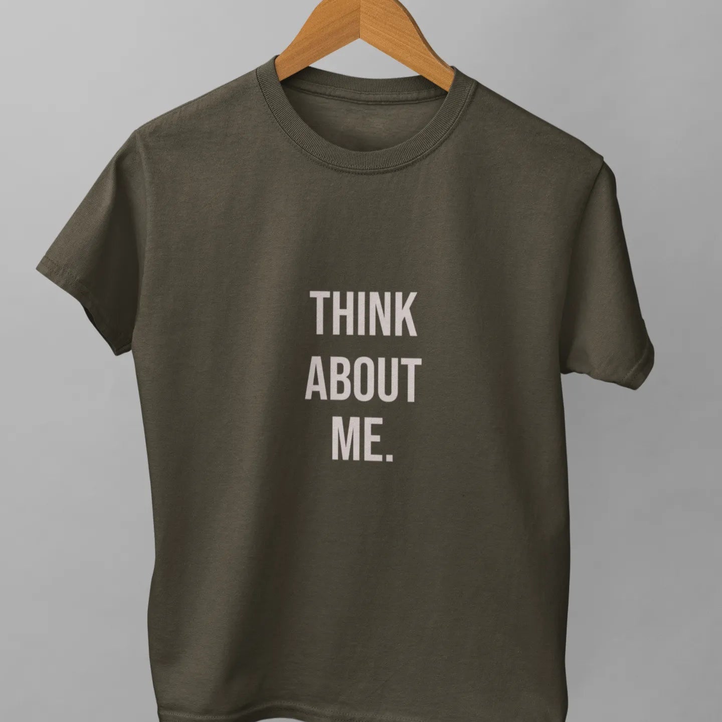 Green t-shirt with 'THINK ABOUT ME.' text on a hanger against a gray background
