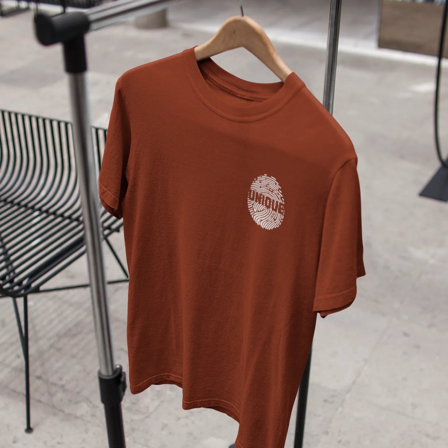 Brown t-shirt with a logo on a hanger against a neutral background