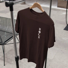 Brown t-shirt with 'MOON' logo on a hanger against a blurred indoor background