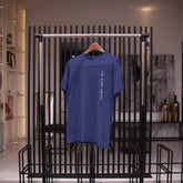 Blue t-shirt on a hanger against a black metal rack in an indoor setting.