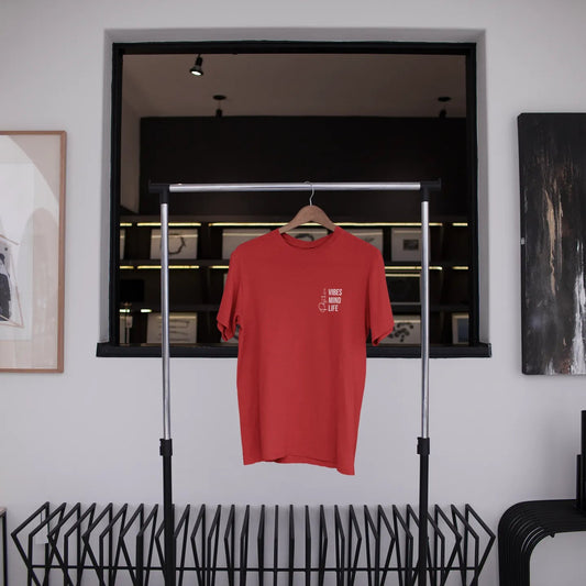 Red t-shirt hanging on a rack in a room with abstract art and a window.
