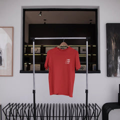 Red t-shirt hanging on a rack in a room with abstract art and a window.