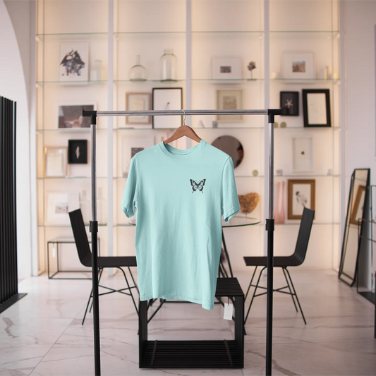 Light blue t-shirt with a butterfly design on a black rack in a modern interior setting.