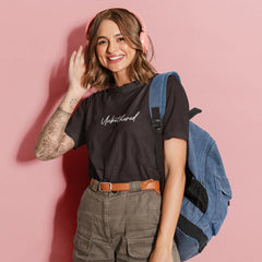 Woman wearing a black t-shirt with text, green cargo shorts, and a blue backpack on a pink background