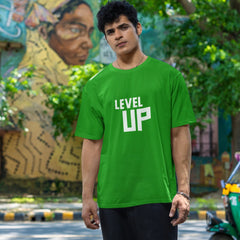 Person wearing a green 'LEVEL UP' t-shirt standing outdoors with trees and a mural in the background.