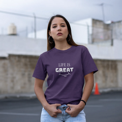Woman wearing a purple t-shirt with 'LIFE IS GREAT' text in an outdoor setting.